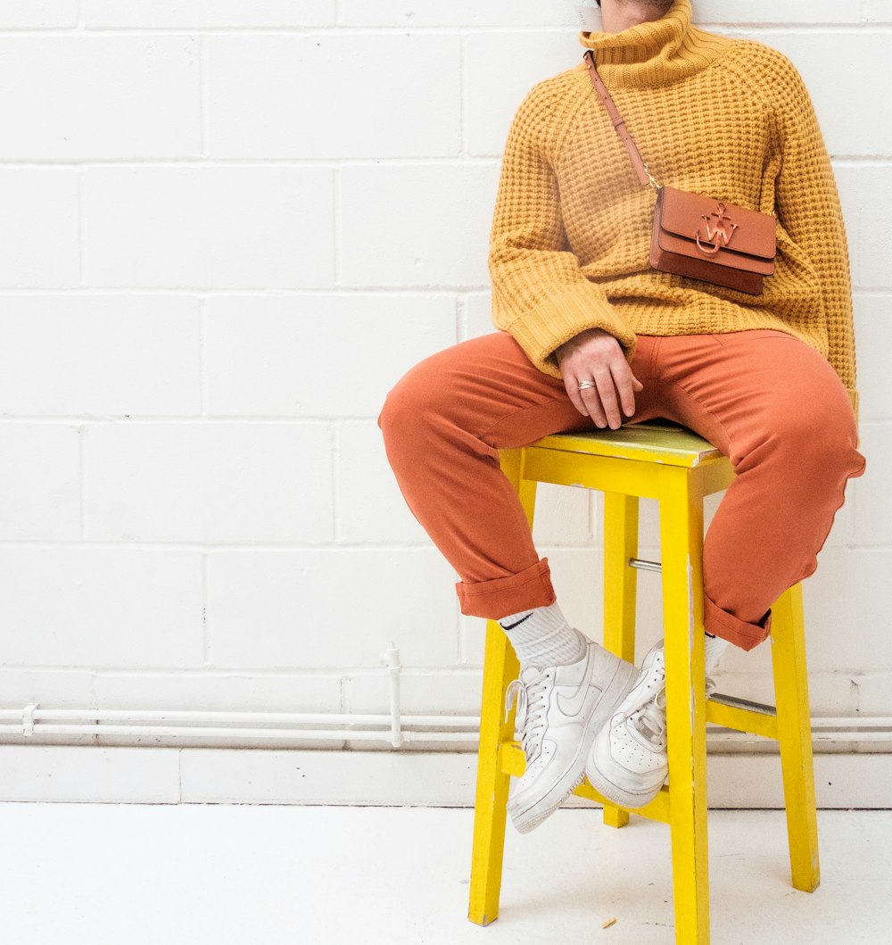 黄色いプラスチックの椅子に座っている茶色のセーターとオレンジ色のズボンを着た男性