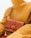 A person wearing a textured mustard yellow turtleneck sweater is holding a brown leather handbag with a unique emblem design on the front. The setting is minimalistic, with a focus on the fashion items.