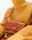 A person wearing a textured mustard yellow turtleneck sweater is holding a brown leather handbag with a unique emblem design on the front. The setting is minimalistic, with a focus on the fashion items.