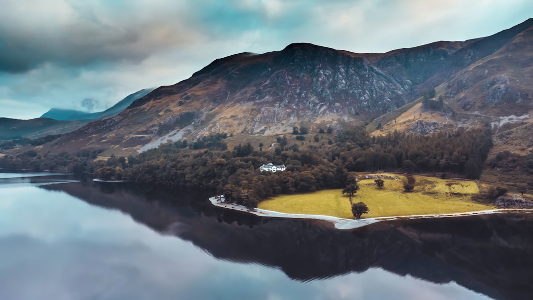 green and brown mountain beside lake under blue sky during daytime