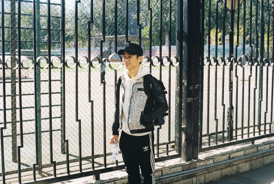 man in black jacket standing beside black metal gate during daytime