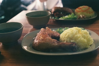 A rustic wooden table with a plate of roasted chicken, rice, and fresh salad.