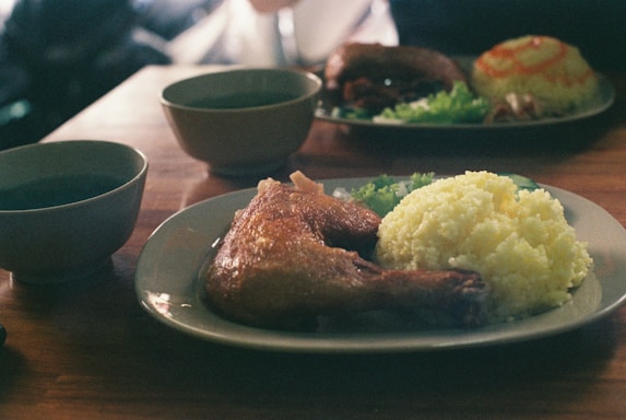 A rustic wooden table with a plate of roasted chicken, rice, and fresh salad.