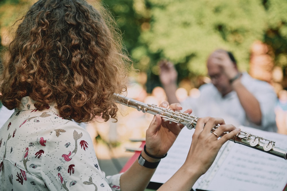 mujer con camisa floral blanca, roja y verde tocando la trompeta