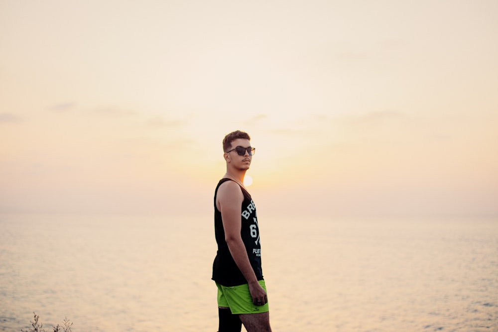 man in black tank top and green shorts standing on beach during daytime