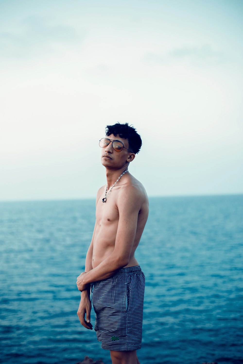 topless man wearing blue and white plaid shorts standing on blue sea during daytime