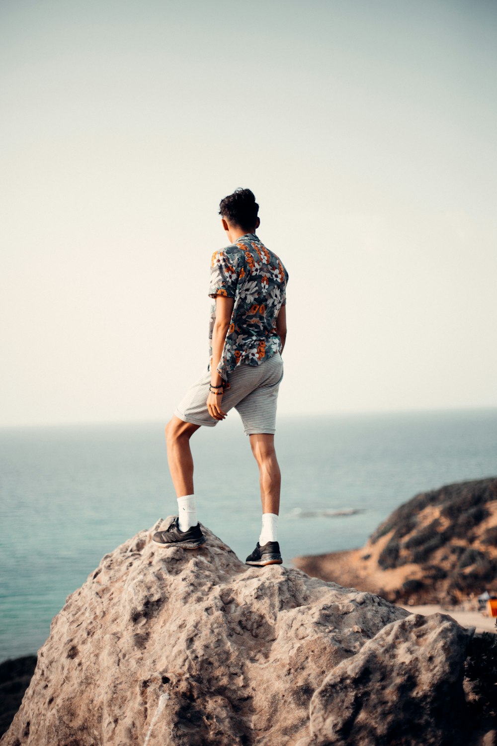 man in blue red and white floral shirt standing on brown rock formation during daytime