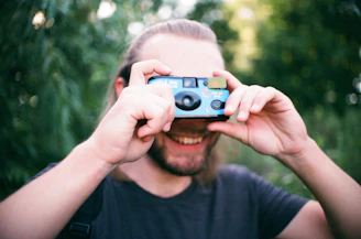 Portrait of Preet Desai holding a camera, smiling against a blurred outdoor background.