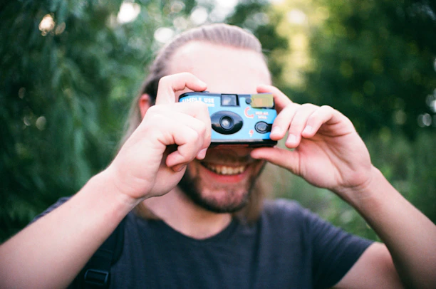 Portrait of Preet Desai holding a camera, smiling against a blurred outdoor background.