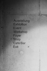A concrete wall with a list of locations and events written in both German and English. The text includes 'Ausstellung', 'Exhibition', 'Event', 'Workshop', 'Foyer', 'Shop', 'Café/Bar', and 'Exit'. An arrow points to the right, indicating direction.