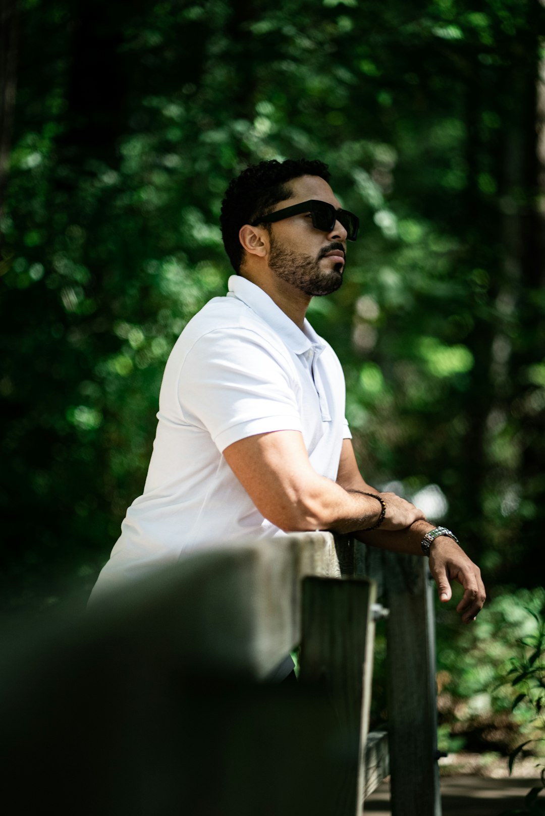 man in white polo shirt and white pants sitting on brown wooden fence during daytime