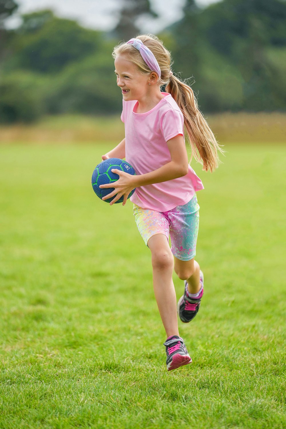girl in pink tank top and pink shorts holding blue soccer ball