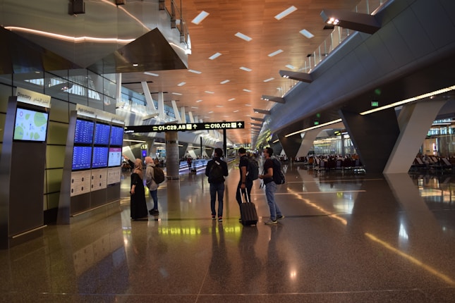 A modern airport terminal with high ceilings and long corridors. Information displays and signboards direct travelers towards gates C1-C29. People are moving with luggage, some checking flight information on the screens.