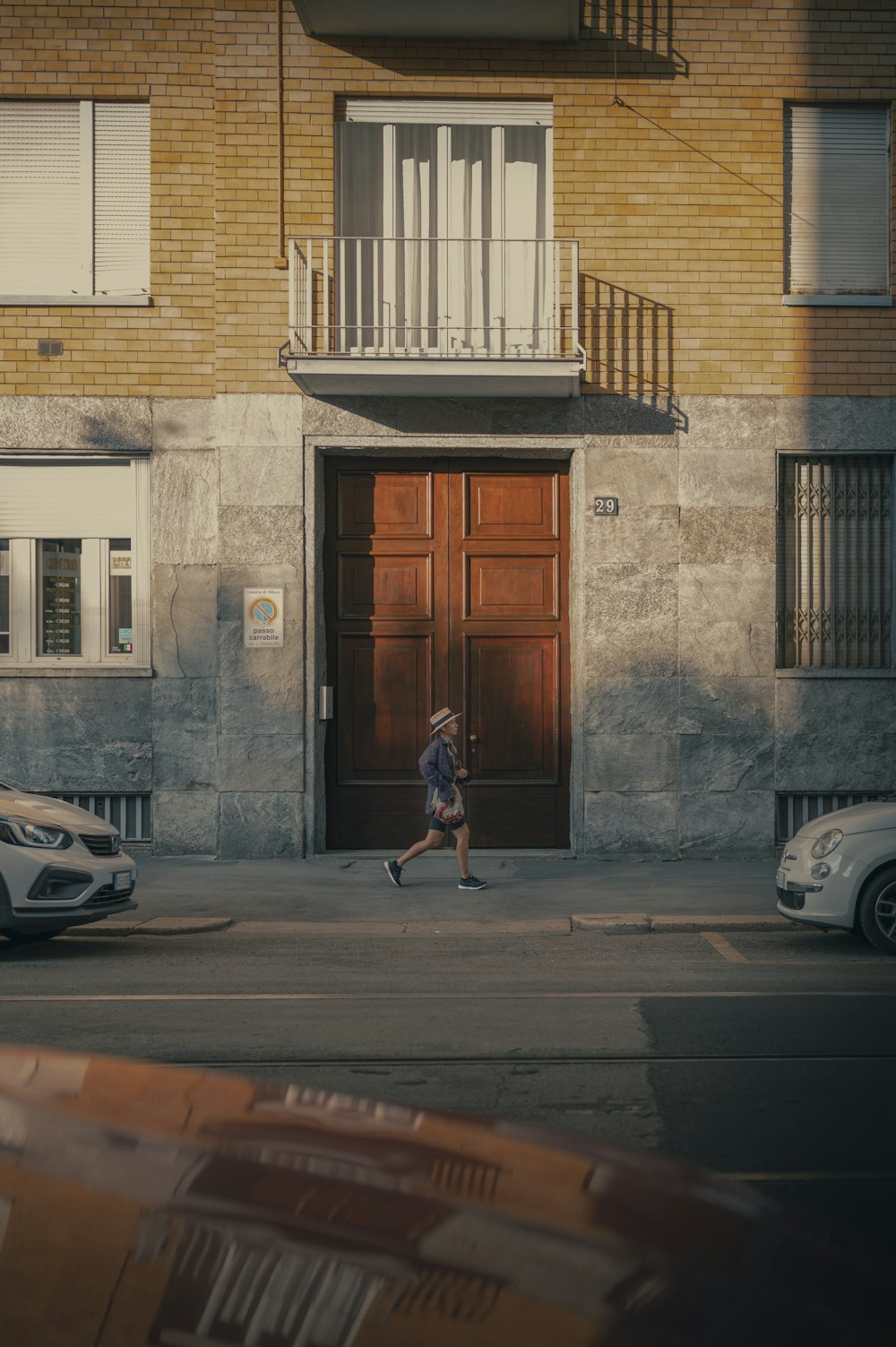 donna in vestito rosso che cammina sul marciapiede vicino alla porta di legno marrone durante il giorno