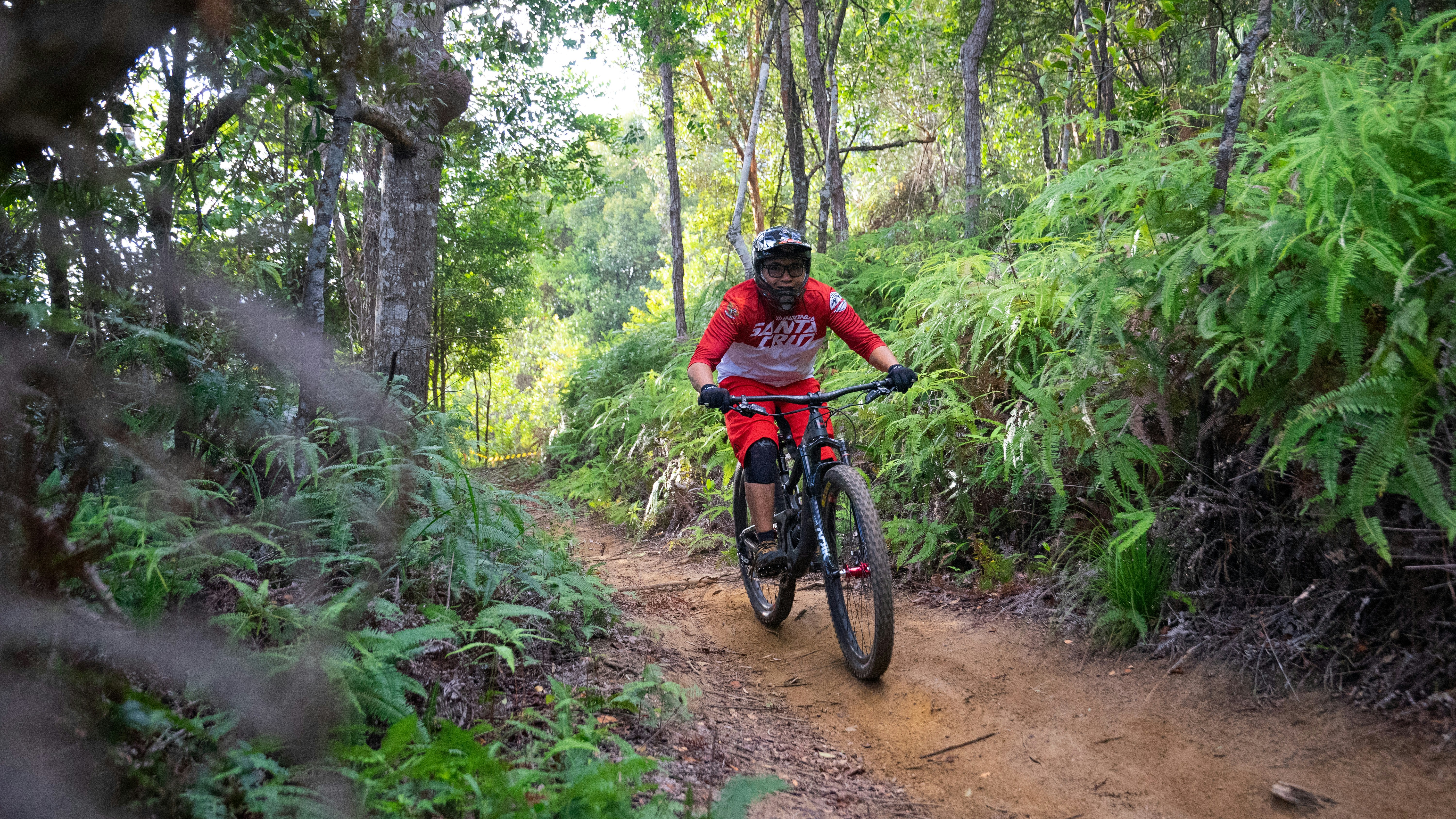 man in red and black shirt riding bicycle on dirt road between green trees during daytime