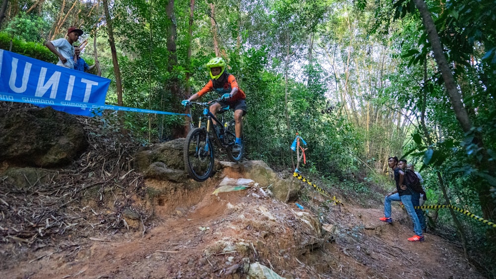 man in green shirt riding mountain bike on brown rocky road during daytime