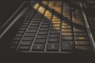 A close-up view of a keyboard with sunlight streaming across it, creating shadows and highlighting certain keys. The keys are dark with a matte finish and there is a recognizable Windows key visible in the image.