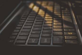 A close-up view of a keyboard with sunlight streaming across it, creating shadows and highlighting certain keys. The keys are dark with a matte finish and there is a recognizable Windows key visible in the image.
