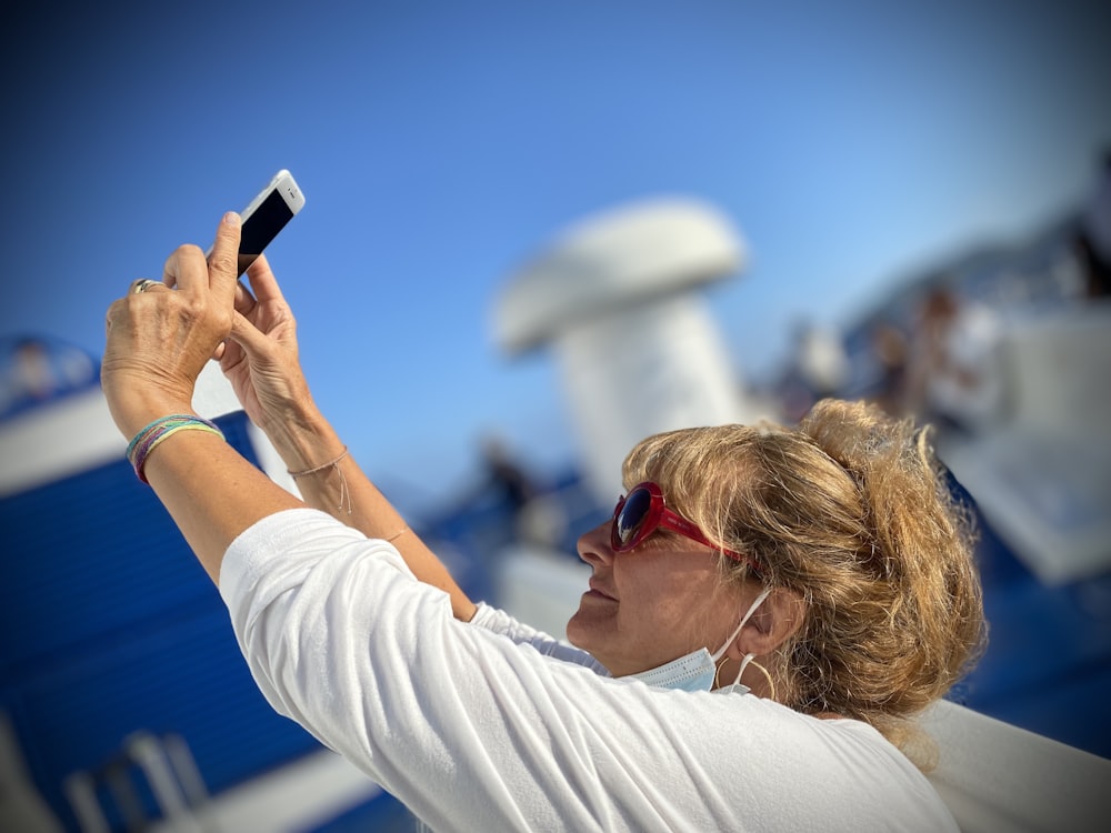 woman in white long sleeve shirt holding smartphone during daytime