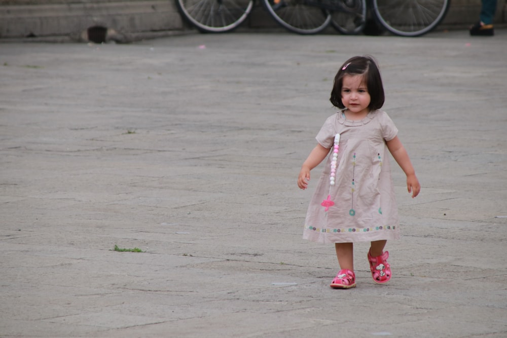 girl in white and pink floral dress standing on gray concrete floor during daytime