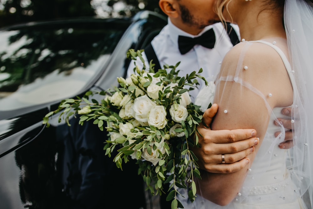 man in black suit holding woman in white wedding dress