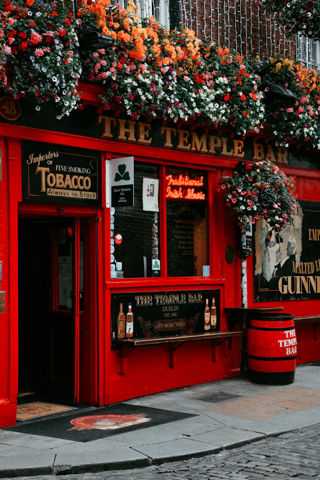 The Temple Bar pub's vivid red facade in Dublin, hung with colourful flower baskets and gold lettering.