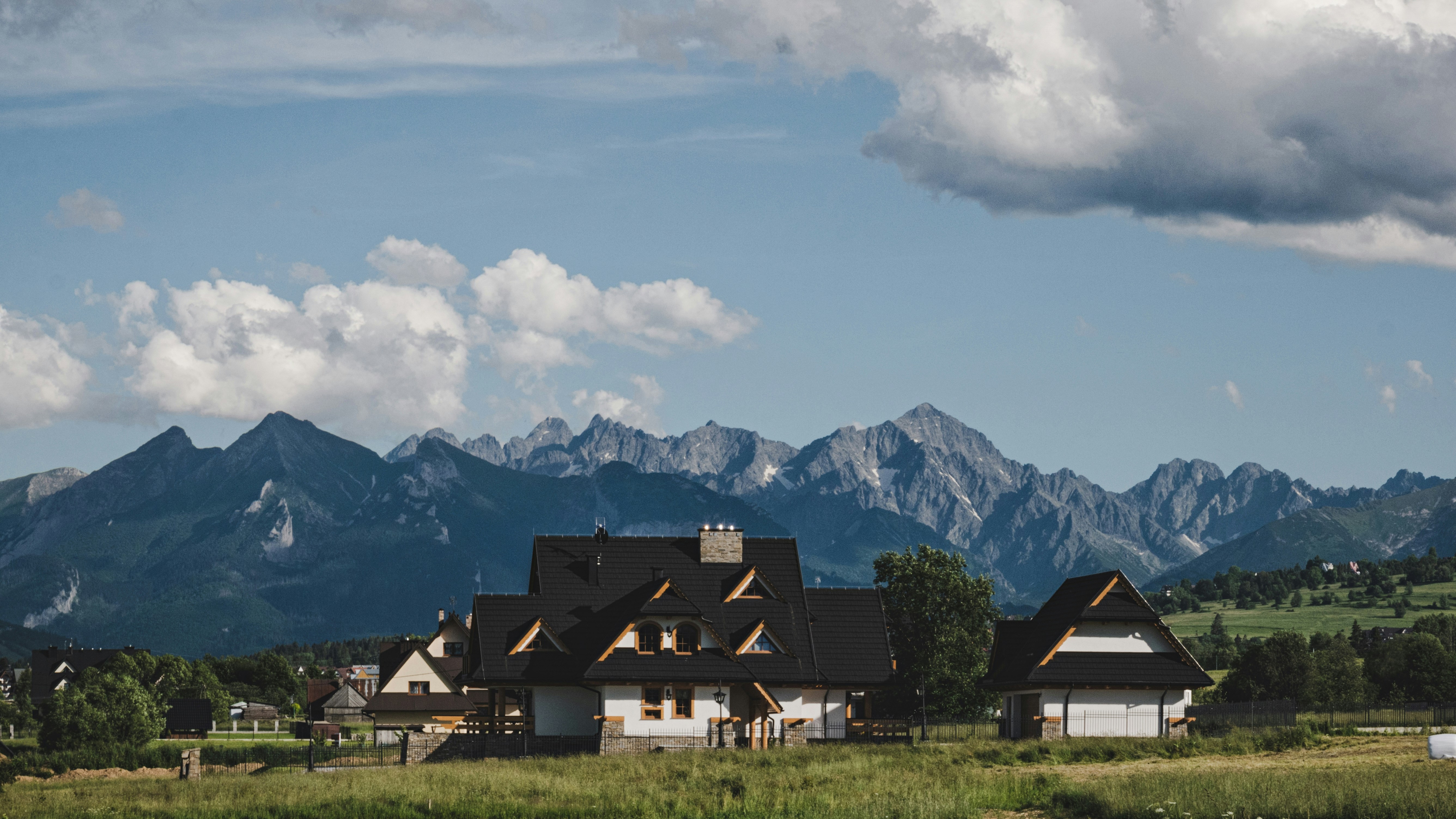 casa preta e branca perto do campo de grama verde e montanha sob nuvens brancas e céu azul