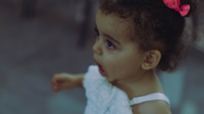 Close-up of a smiling child wearing a bright pink bow and a soft cotton dress.