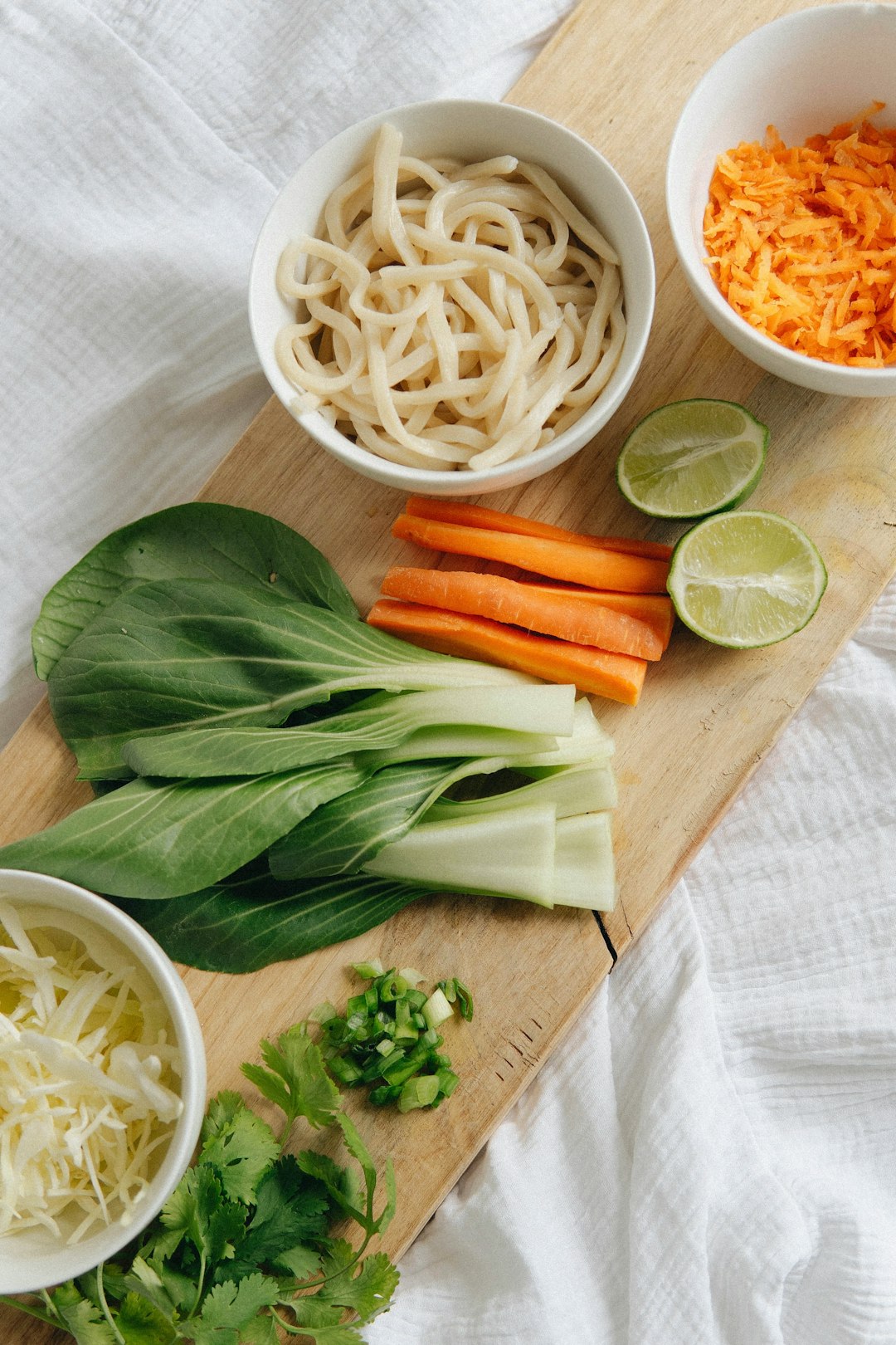 white pasta with carrots and green leaf vegetable on brown wooden chopping board