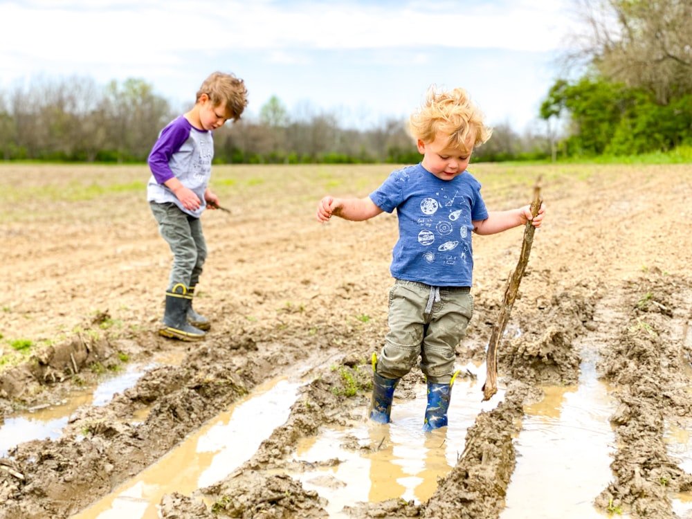 boy in blue t-shirt and brown pants standing on brown soil during daytime