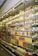 A store aisle featuring a large refrigerated section stocked with a colorful assortment of bottled beverages and packaged fruit cups. The products are neatly arranged on shelves behind glass doors, illuminated by bright indoor lighting.
