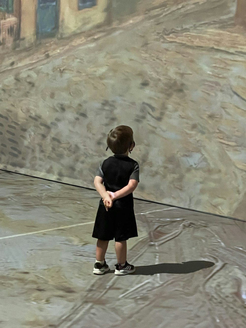 Niño con camiseta negra y pantalones cortos parado sobre arena marrón durante el día