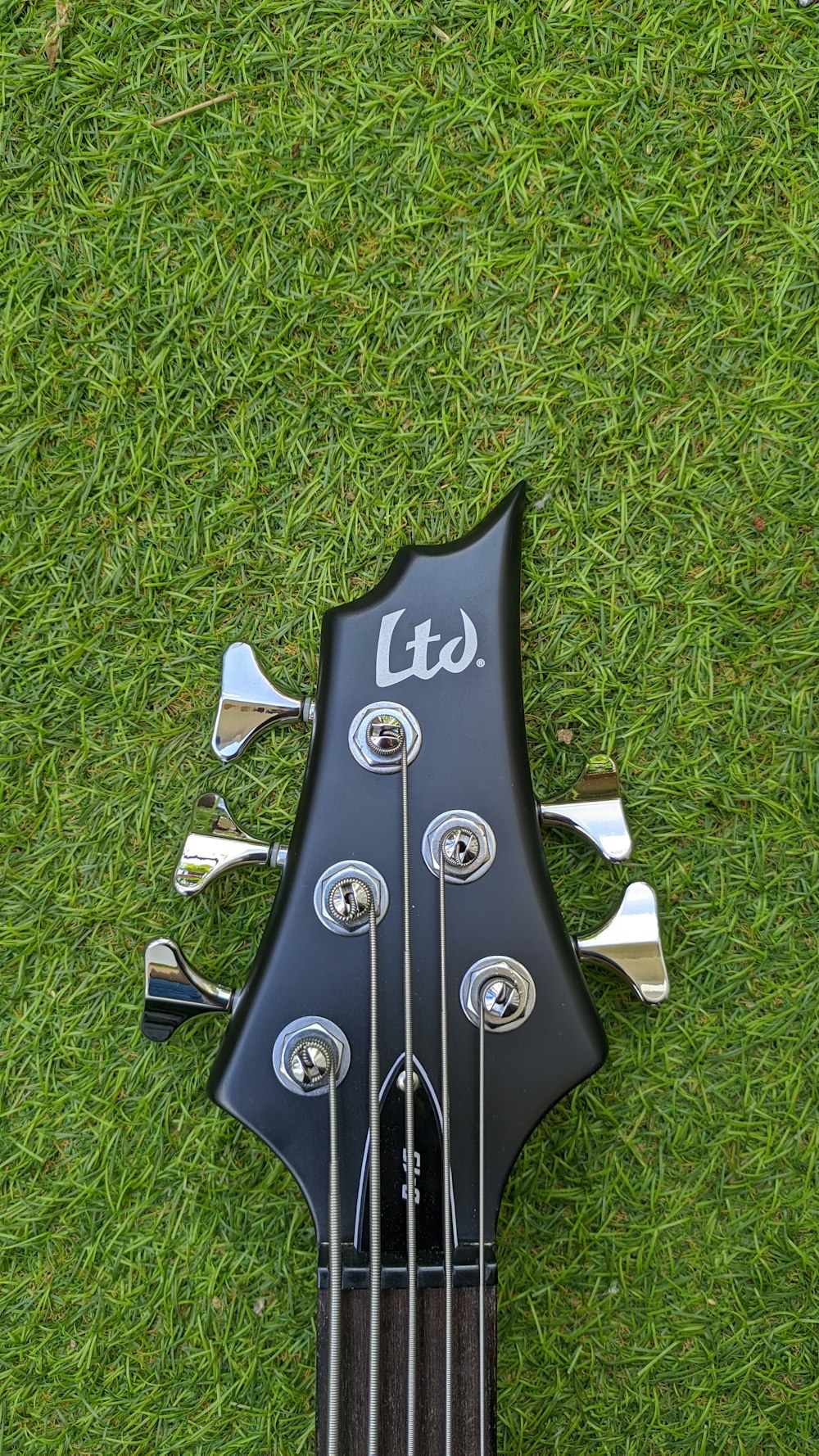 a black guitar laying on top of a lush green field