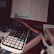A calculator is placed on top of a stack of books, one of which is titled 'Chemistry'. An open book with text and diagrams is positioned in the background, suggesting a study or work environment. There are additional items like a small bottle and a tube nearby.