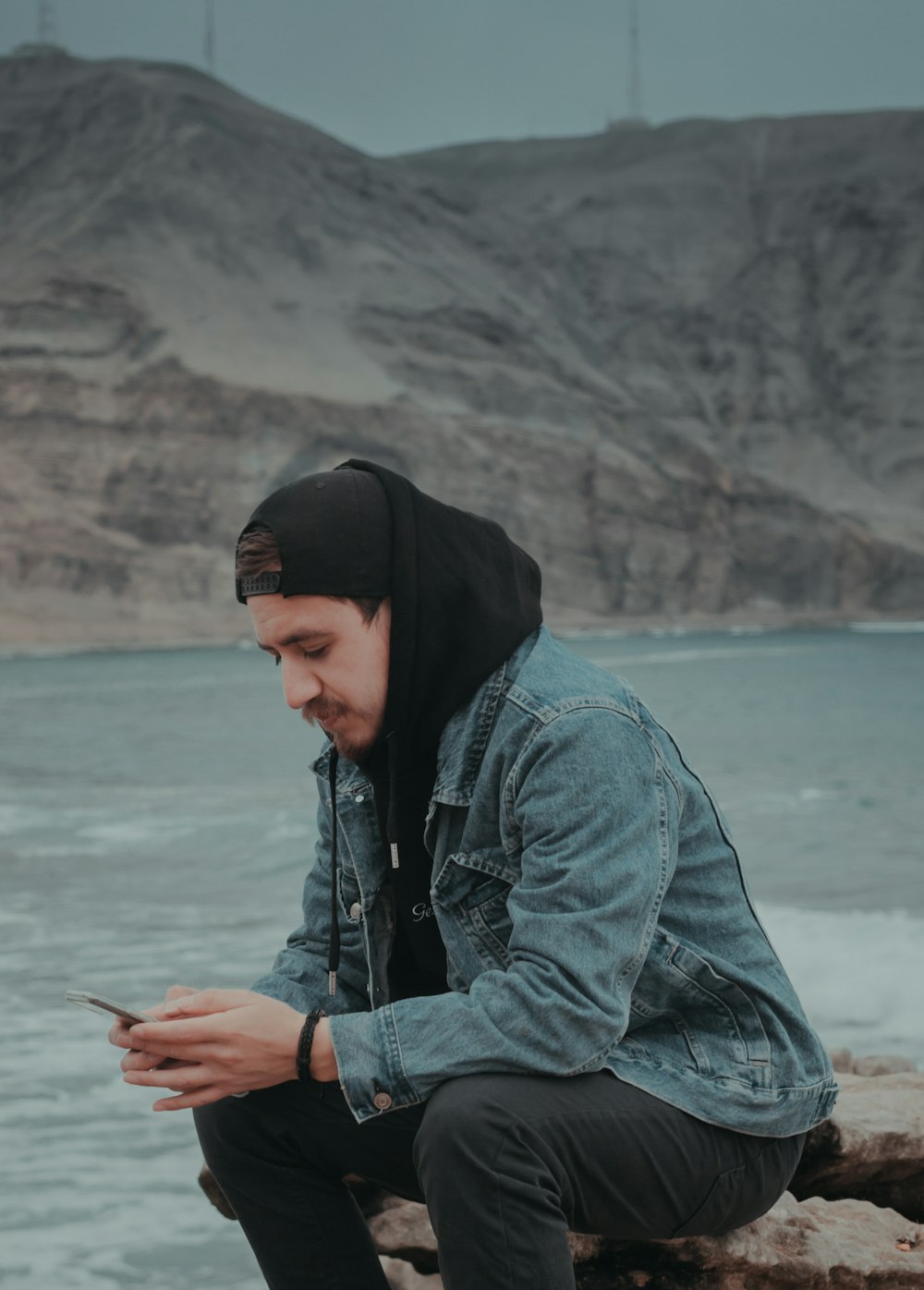 woman in blue denim jacket and black knit cap holding smartphone