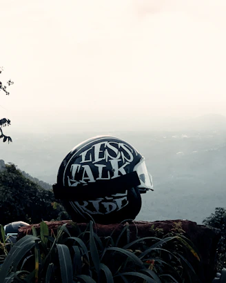 A lightweight helmet resting on a grassy hill with a panoramic view of soaring paragliders.