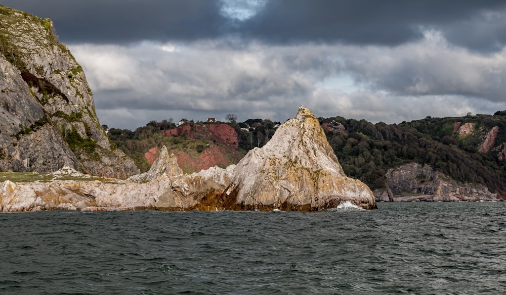 brown rock formation on sea under gray clouds