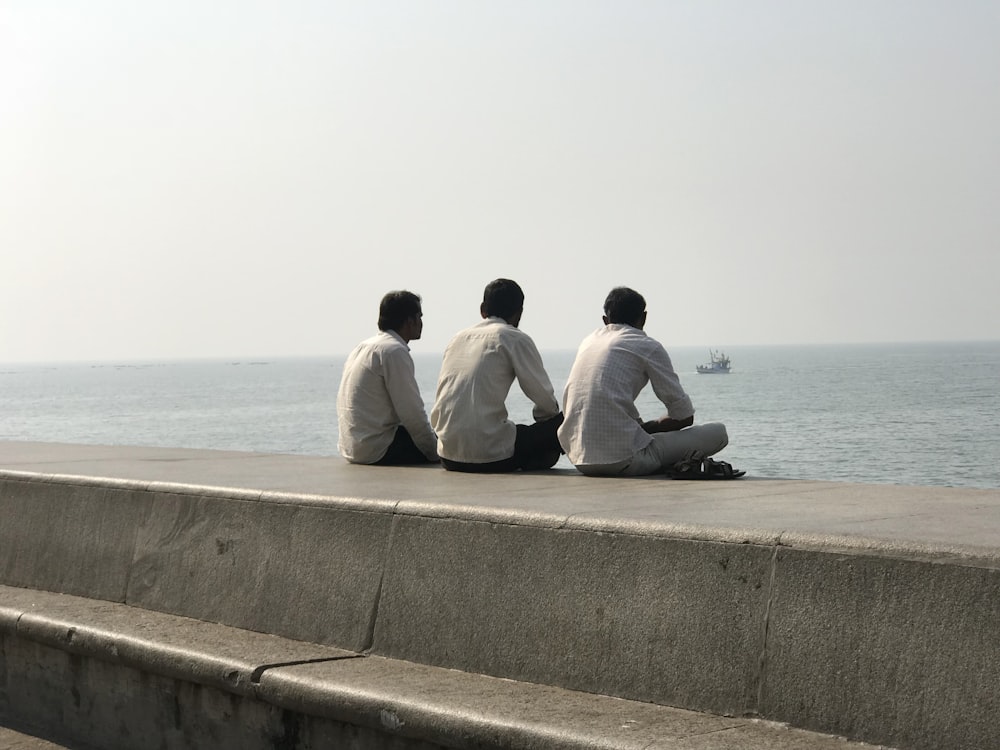 2 men sitting on concrete bench by the sea during daytime