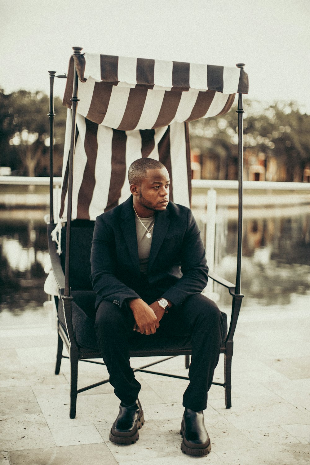 man in black suit sitting on white and blue striped chair