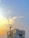 A construction site with a tall crane towering over a partially built structure against a backdrop of a vibrant sky transitioning from warm yellow to a soft blue. The building displays some branding, and the crane is prominently positioned on the left side.