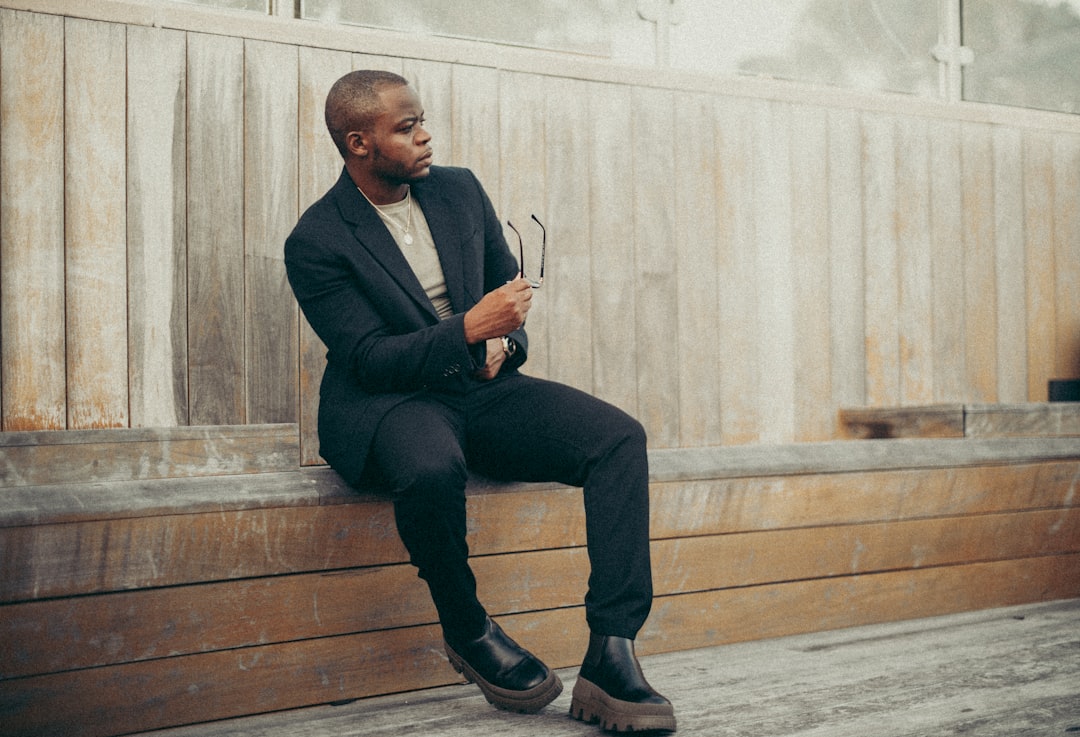 man in black suit jacket and black pants sitting on brown wooden stairs