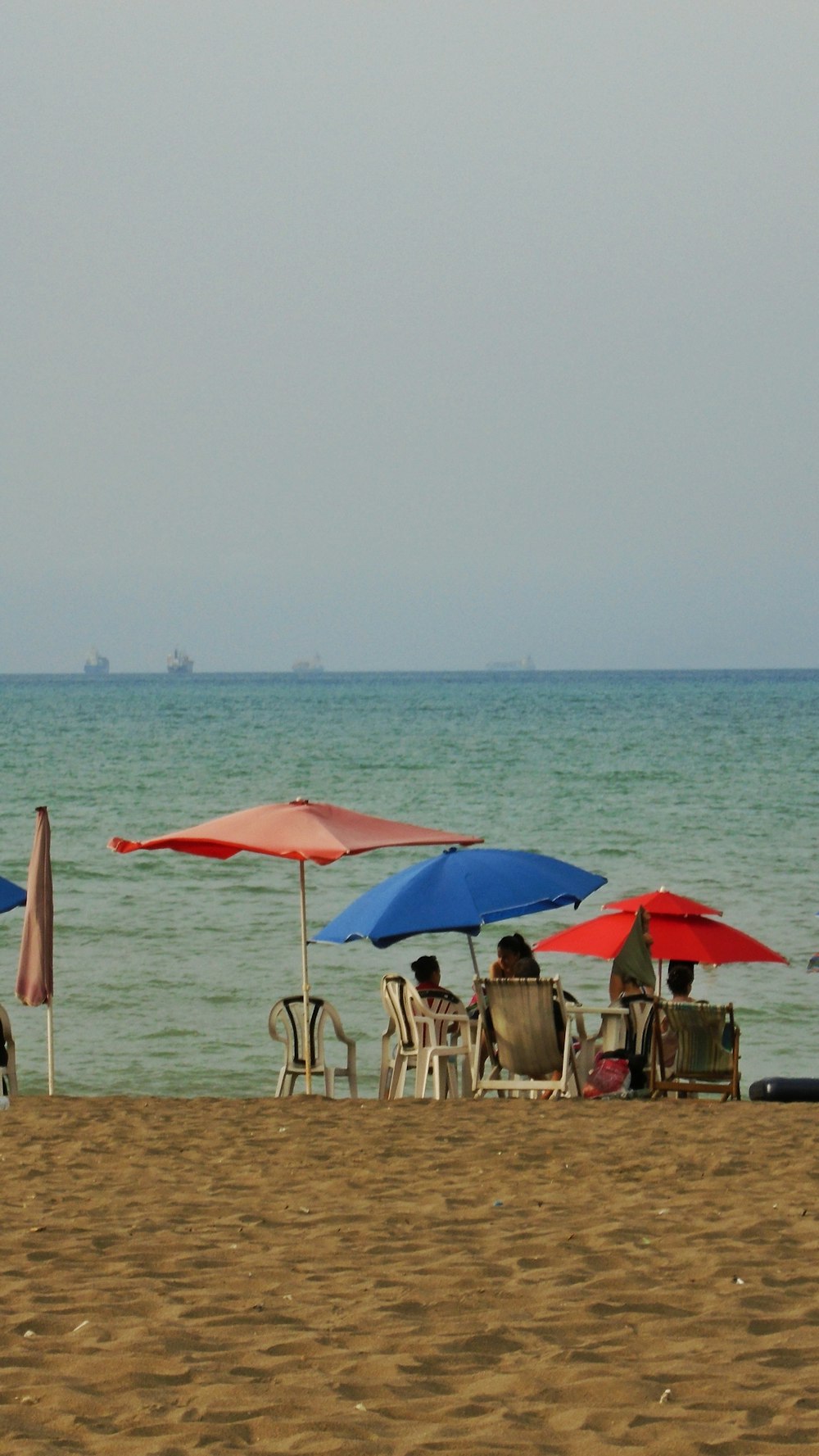 people sitting on beach chairs under red umbrella during daytime