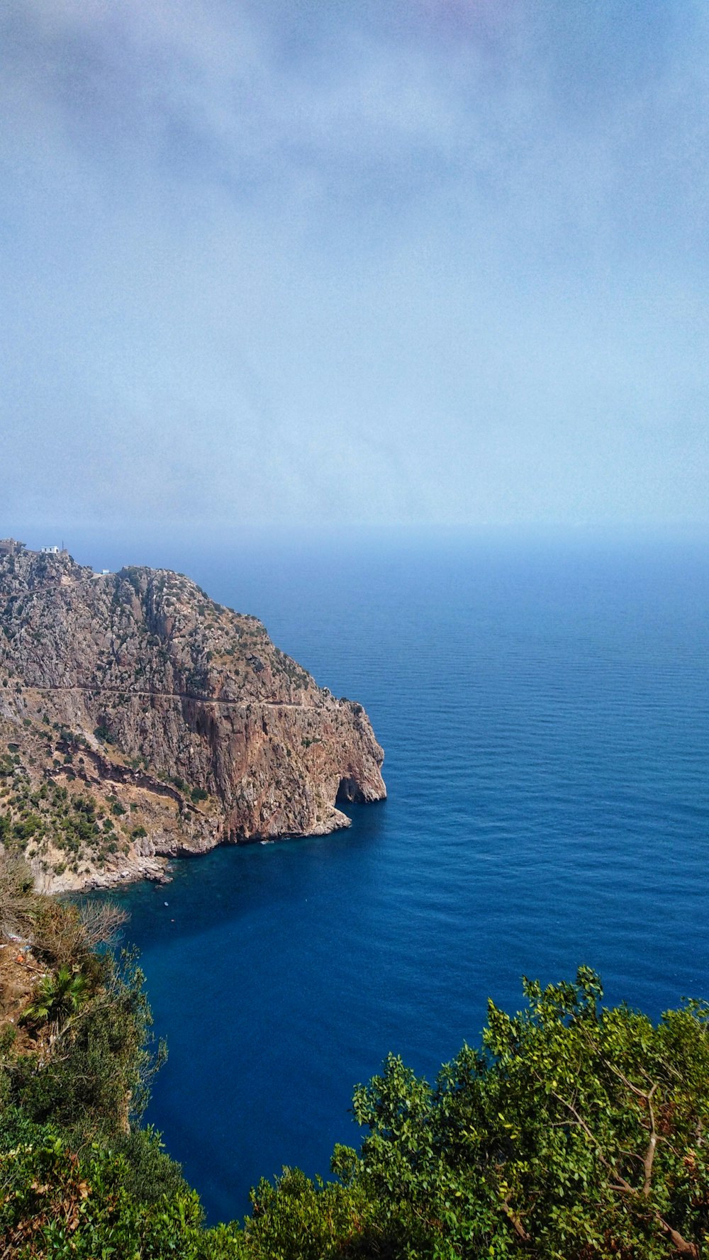 Montaña marrón y verde junto al mar azul bajo el cielo blanco durante el día