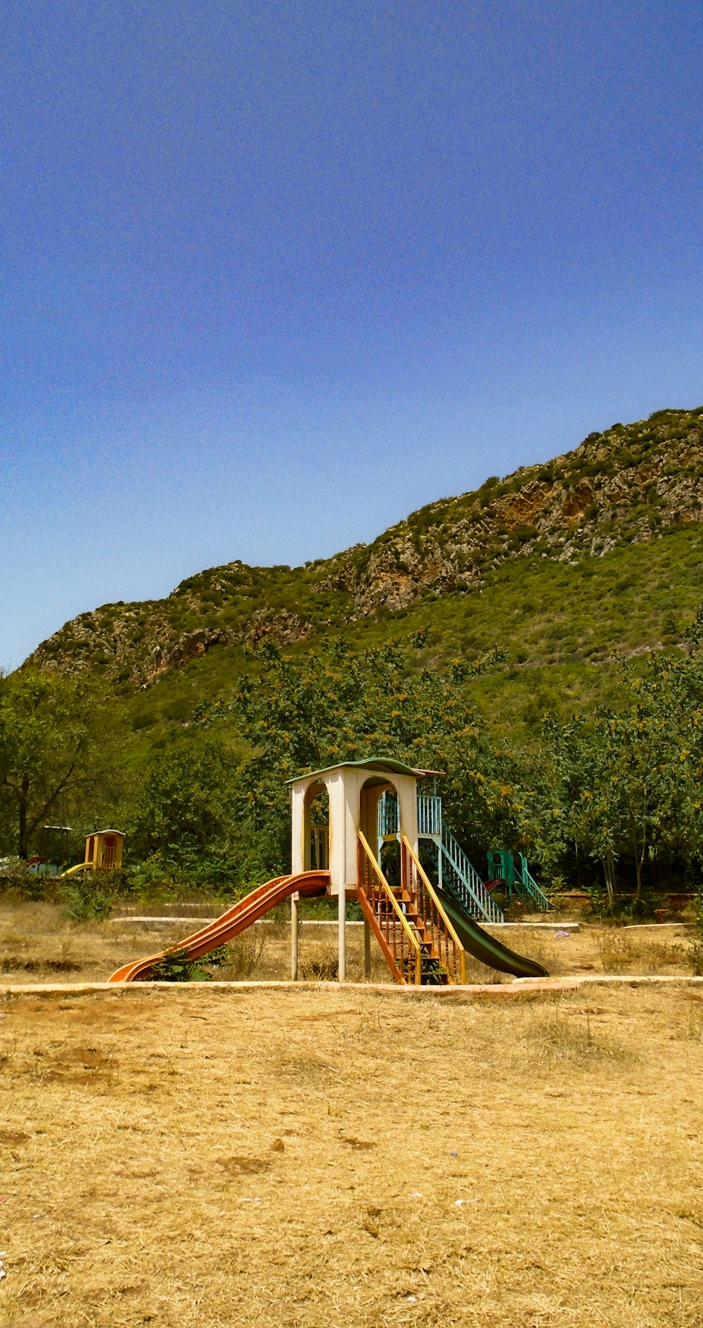 blue and brown wooden playground near green mountain under blue sky during daytime