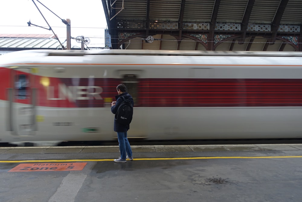 man in black jacket standing beside red and white train