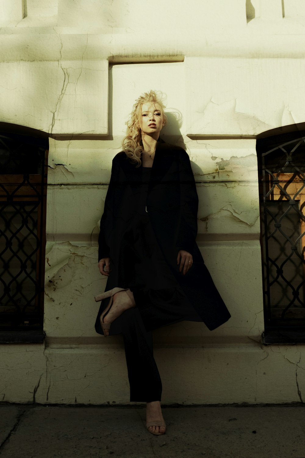 woman in black coat sitting on white concrete wall