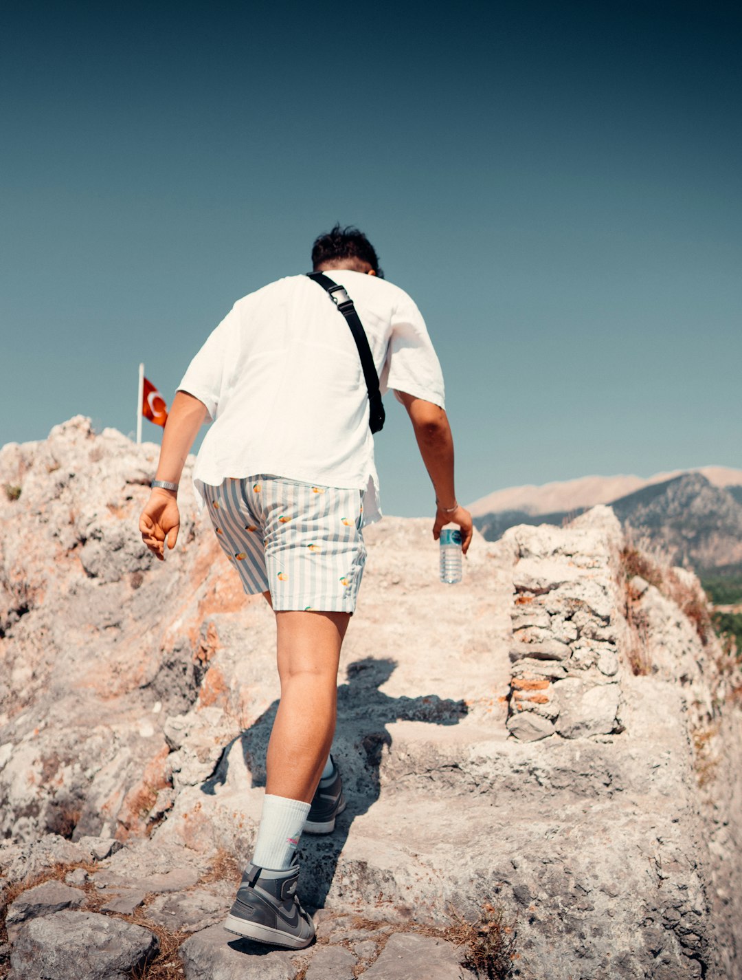 man in white t-shirt and brown plaid shorts standing on rocky hill during daytime