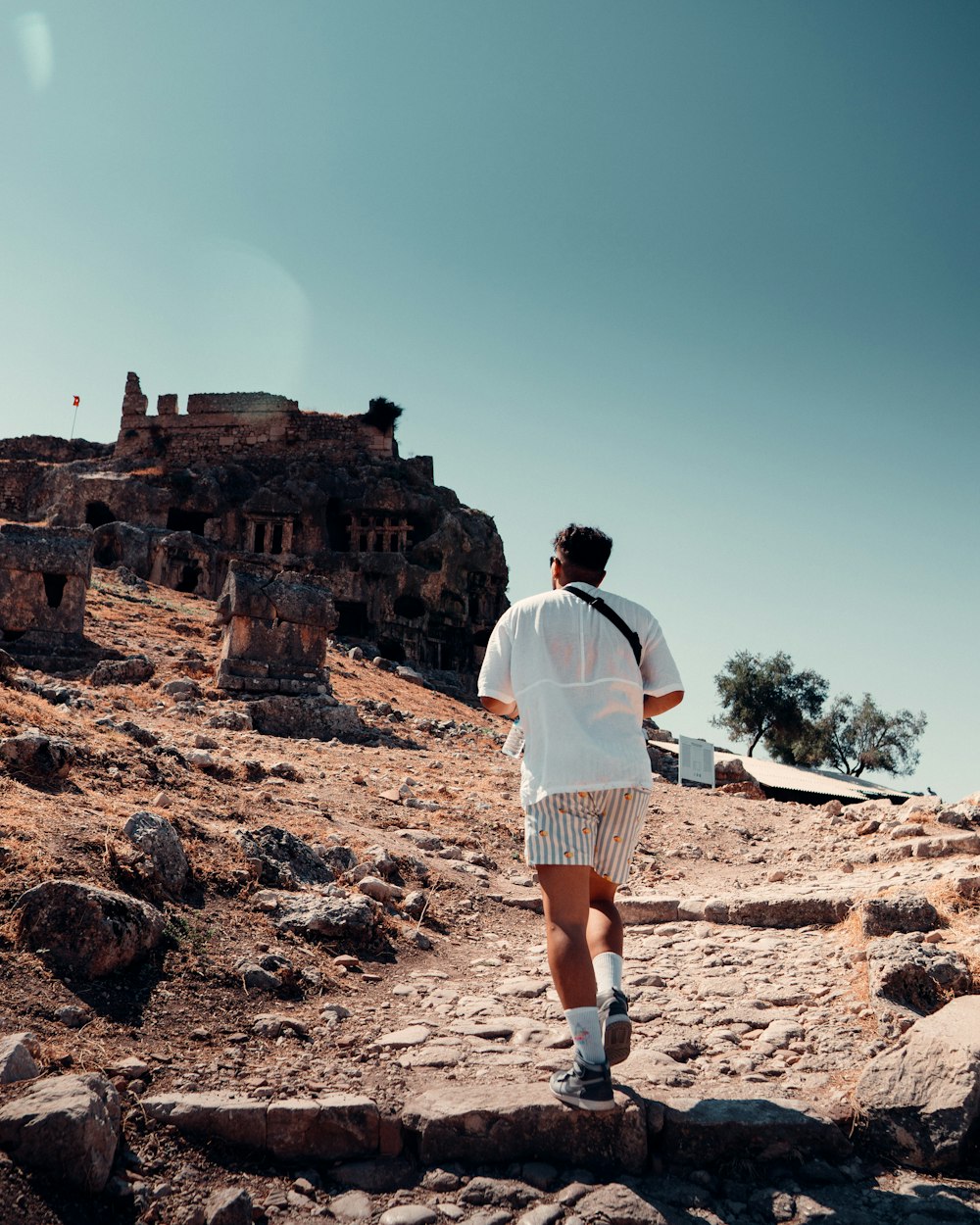 man in white shirt and white shorts standing on brown rock formation during daytime