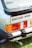 The image depicts the rear section of a vintage Ford Escort XR3, showcasing its distinctive tail lights and branding. The logo is prominently displayed, highlighting its classic design with a sleek black spoiler and visible exhaust pipe. The vibrant red and orange of the tail lights add a retro appeal.