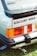 The image depicts the rear section of a vintage Ford Escort XR3, showcasing its distinctive tail lights and branding. The logo is prominently displayed, highlighting its classic design with a sleek black spoiler and visible exhaust pipe. The vibrant red and orange of the tail lights add a retro appeal.